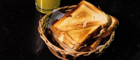 A sandwich in a basket and a glass of juice on a dark surface.
