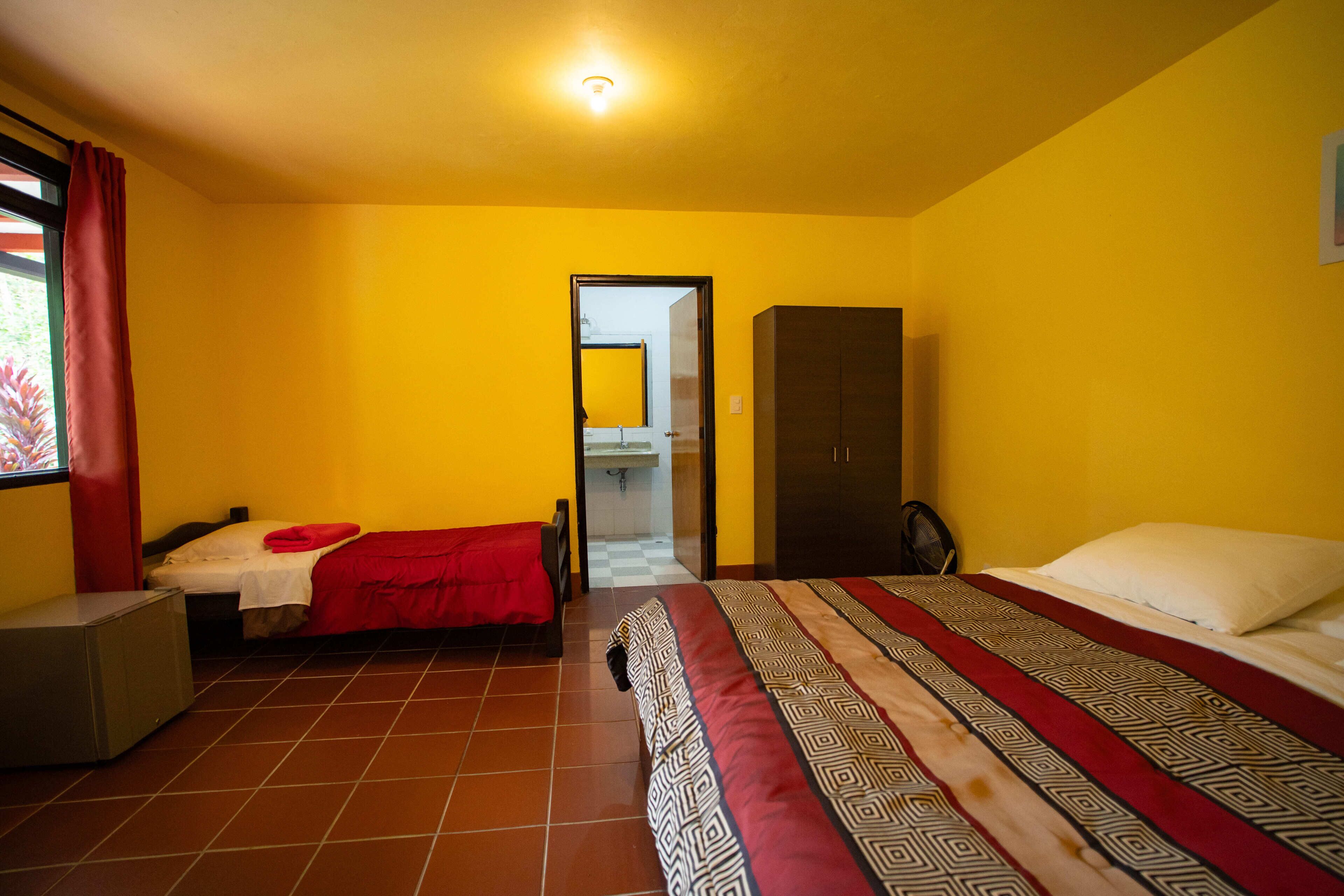 Une chambre avec deux lits, une armoire, un bureau et une fenêtre avec des rideaux.