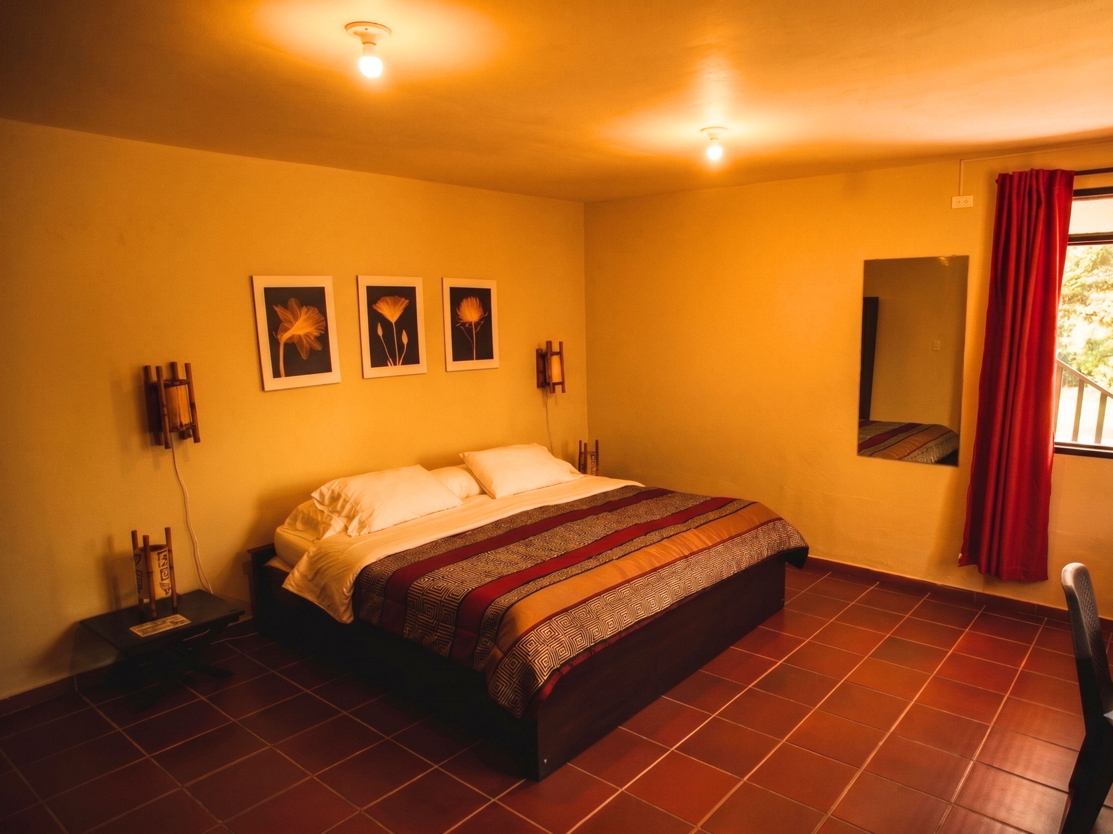 Un dormitorio con cama, una lámpara de pared, un espejo y una ventana con cortinas.