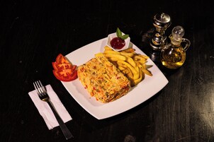 Un plato con una rodaja de tomate, un trozo de comida frita y papas fritas, acompañado de un recipiente pequeño de kétchup y dos salsas en una mesa oscura.