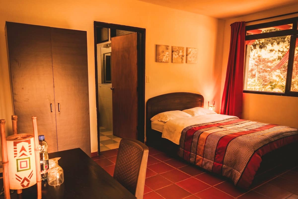 Una habitación con cama, una mesa con sillas, un armario y una ventana con cortinas.