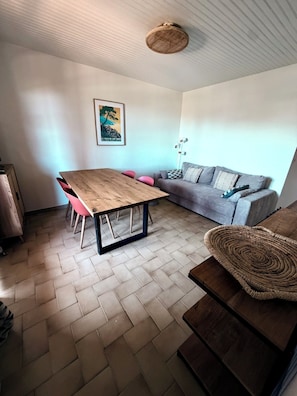 Ein Zimmer mit einem Holztisch, rosa Stühlen, einem grauen Sofa und einem gewebten Korb.