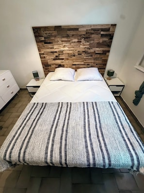 Ein Bett mit hölzernem Kopfteil, weißer Bettwäsche und einer gestreiften Tagesdecke.