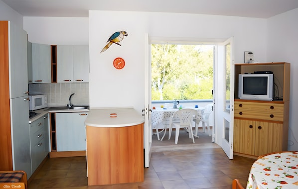 Cocina pequeña con microondas, lavamanos y encimera de madera, que da a un balcón con mesa y sillas.