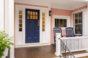 A house with a blue door, white porch railing, and a brick wall.