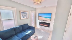 Un salon avec un canapé bleu, un téléviseur à écran plat, une cheminée et une œuvre d’art encadrée accrochée au mur.