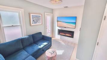 A living room with a blue sofa, a flat-screen TV, a fireplace, and a framed artwork on the wall.