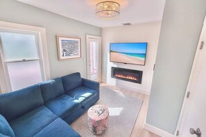 Ein Wohnzimmer mit blauem Sofa, Flachbildfernseher, Kamin und einem gerahmten Kunstwerk an der Wand.
