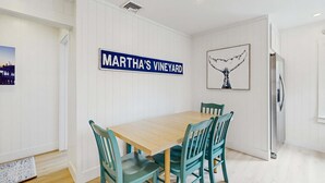 Un coin repas avec une table en bois et des chaises de couleur turquoise, une enseigne indiquant « MARTHA’S VINEYARD », et une œuvre d’art représentant une baleine, encadrée, accrochée au mur.