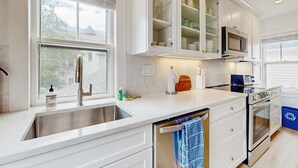 Une cuisine moderne dotée d’un évier en acier inoxydable, de meubles blancs, d’un four à micro-ondes encastré et d’un four traditionnel.