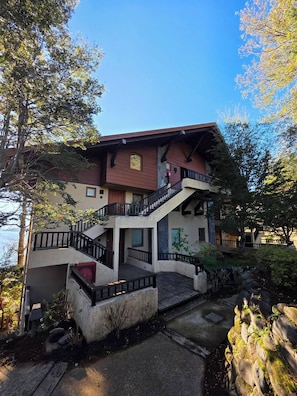 A two-story building with a balcony, a staircase, and a view of the surrounding trees.