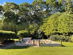 Ein Garten mit erhöhten Beeten, einer hölzernen Bank und verschiedenen Bäumen und Sträuchern.