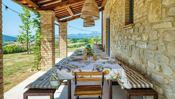 Un espace de restauration en plein air avec une table dressée pour deux personnes, des murs en pierre et une vue sur la campagne.