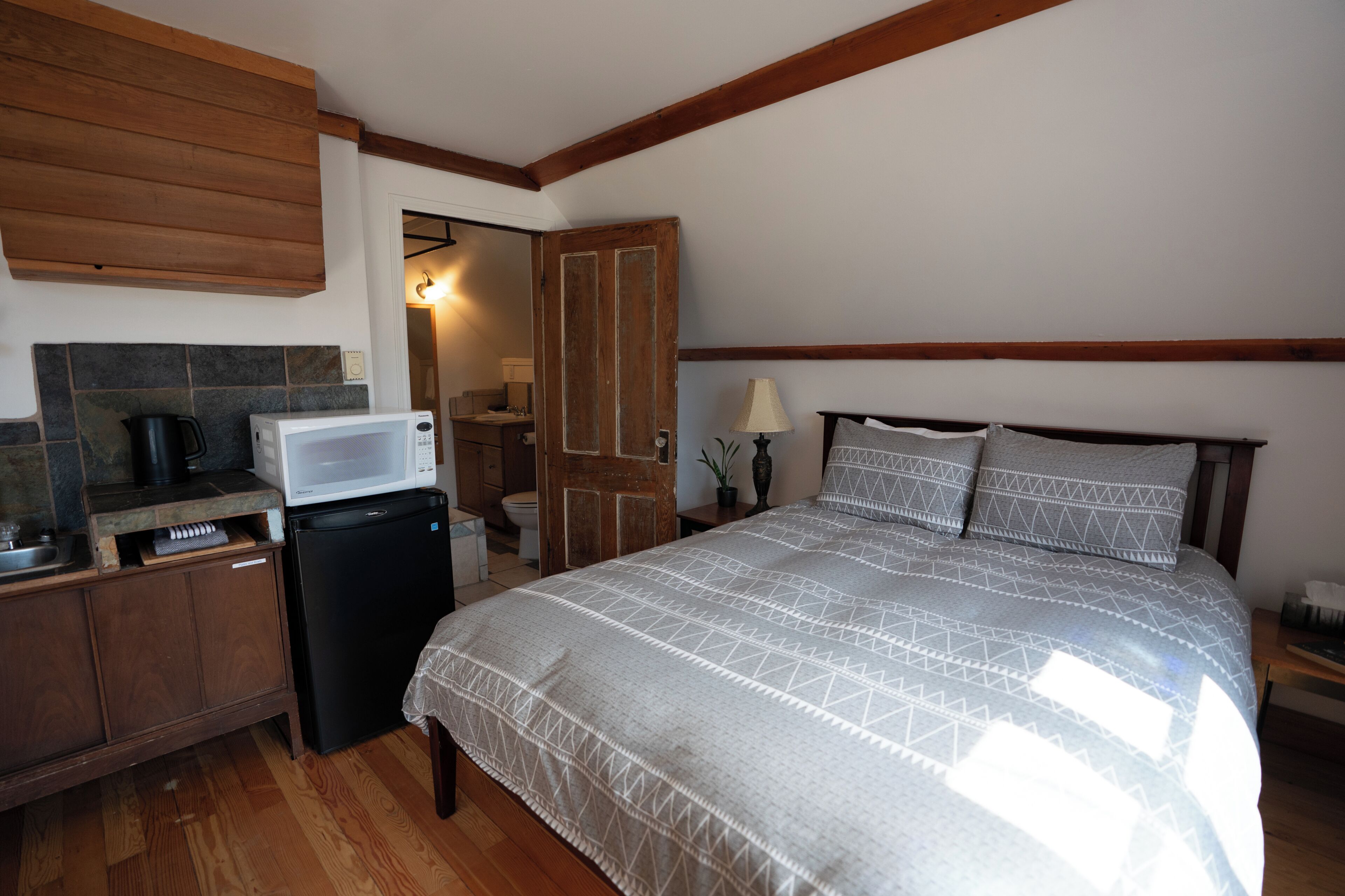 A bedroom with a bed, a nightstand, a dresser, a microwave, and a refrigerator.