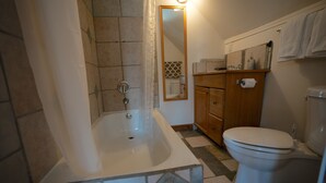 A bathroom with a bathtub, toilet, and a wooden cabinet. - Kaslo Manor Lodge - The Garden Suite (Kaslo)