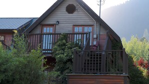A wooden house with a gabled roof, a front porch, and a small garden area. - Kaslo Manor Lodge - The Garden Suite (Kaslo)