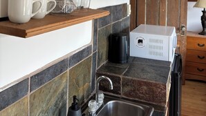 A kitchen with wooden cabinets, a coffee maker, and various kitchen items on shelves. - Kaslo Manor Lodge - The Garden Suite (Kaslo)