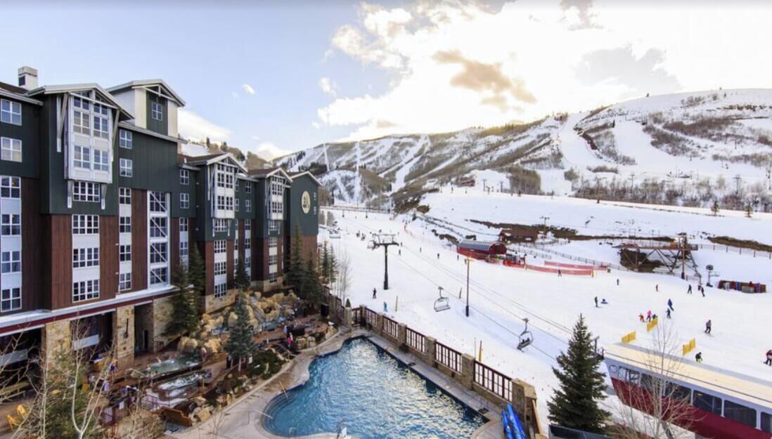 Un hotel con piscina, pista de esquí y montañas al fondo.