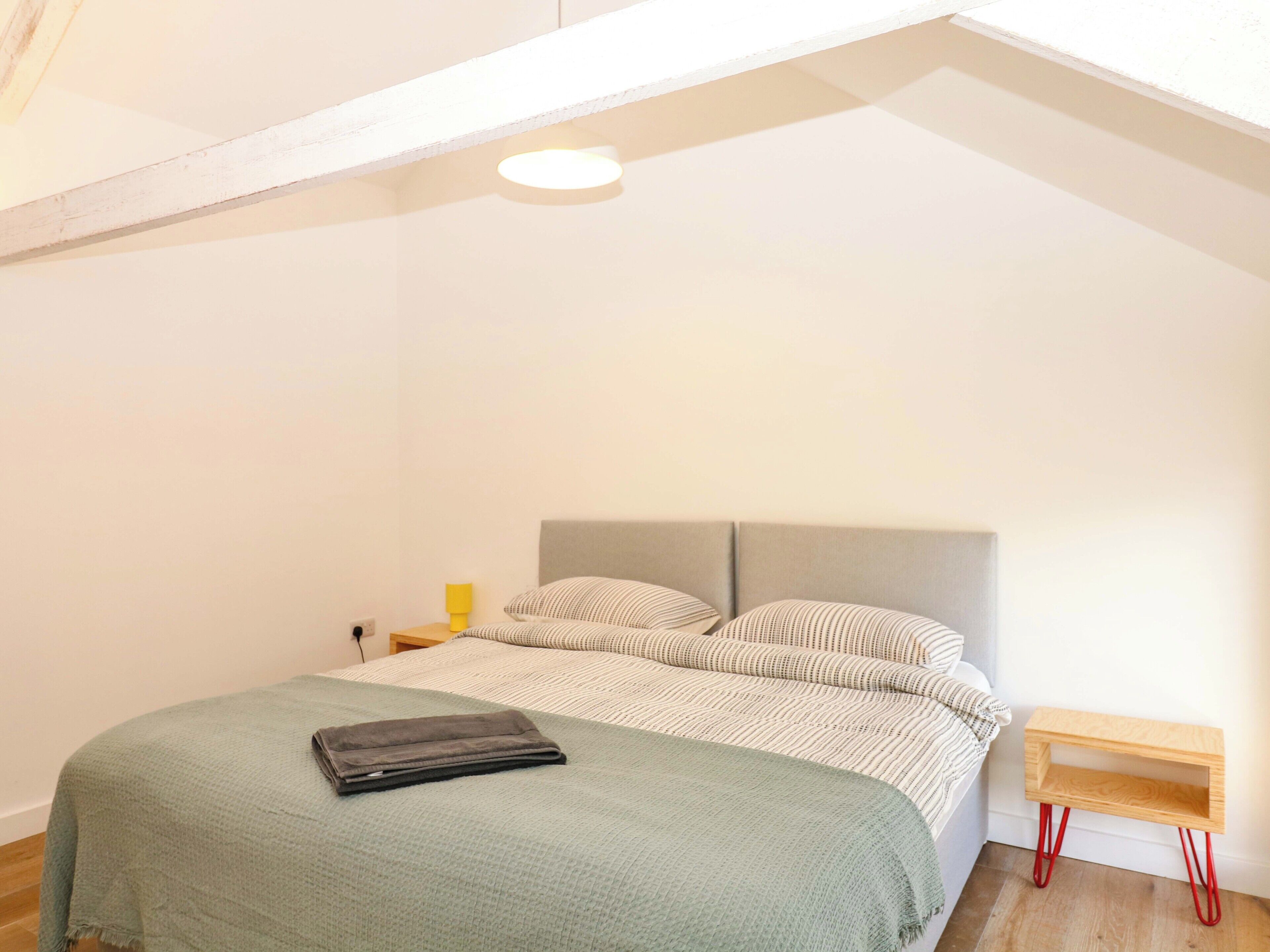 A bedroom with a bed, a bedside table, a lamp, and a wooden nightstand.