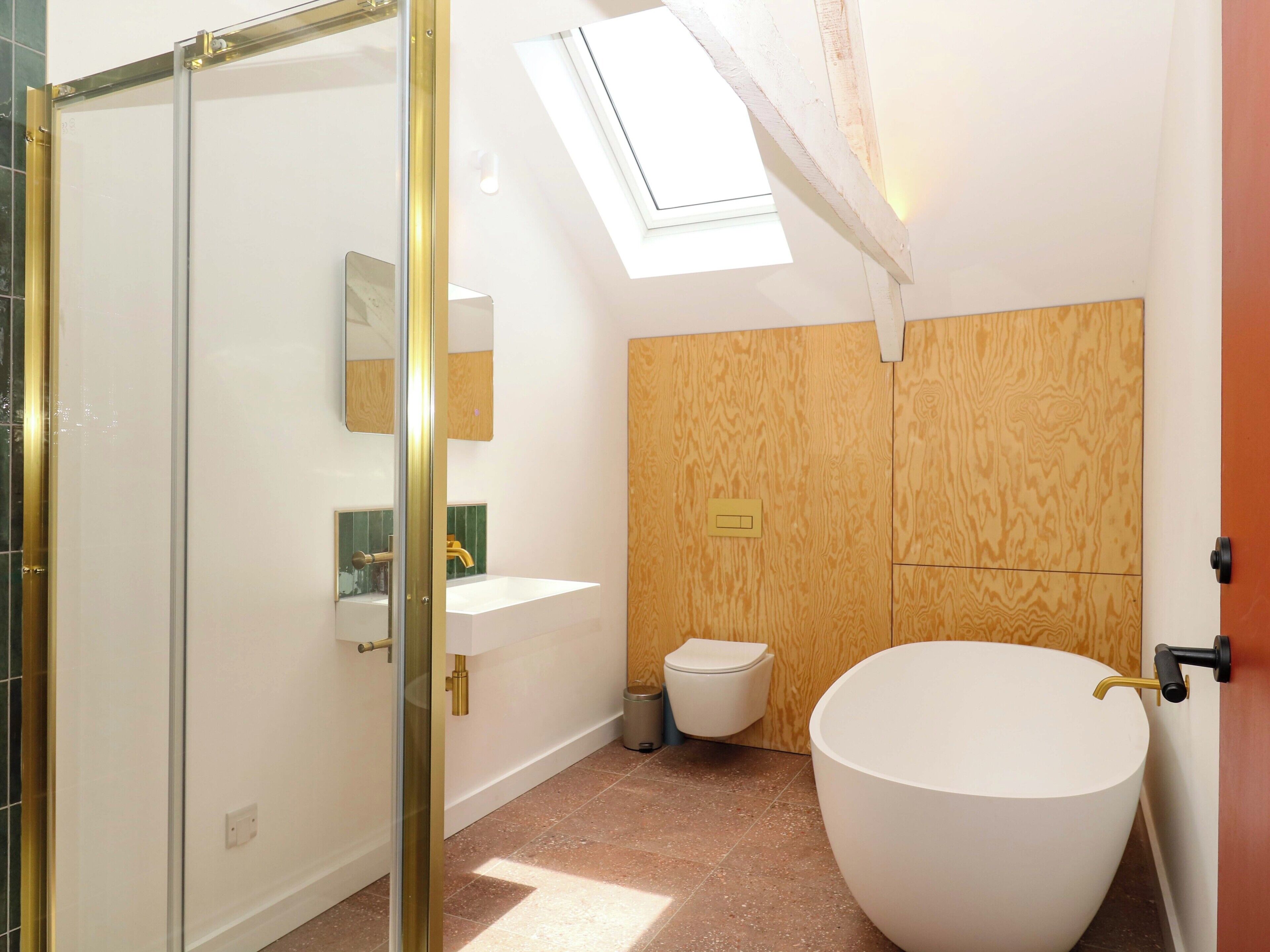 Een moderne badkamer met een vrijstaand ligbad, een douchecabine met glazen wanden en een dakraam.
