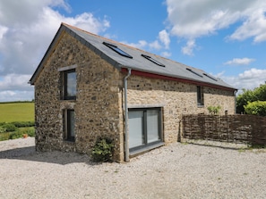 A stone building with a sloped roof, a gravel driveway, and a wooden fence. - Reddaway Byre (Okehampton)