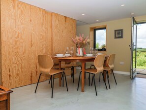A dining area with a wooden table, six chairs, and a vase with flowers. - Reddaway Byre (Okehampton)
