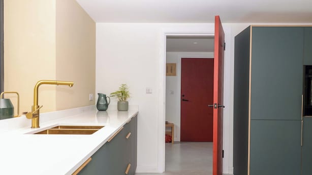 Une cuisine moderne avec un plan de travail blanc, un robinet doré et des armoires vertes.