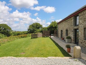 A stone building with a paved patio, a grassy lawn, and a stone wall. - Reddaway Byre (Okehampton)