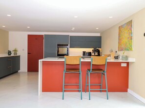 A modern kitchen with a central island, two bar stools, a microwave, and a coffee machine. - Reddaway Byre (Okehampton)