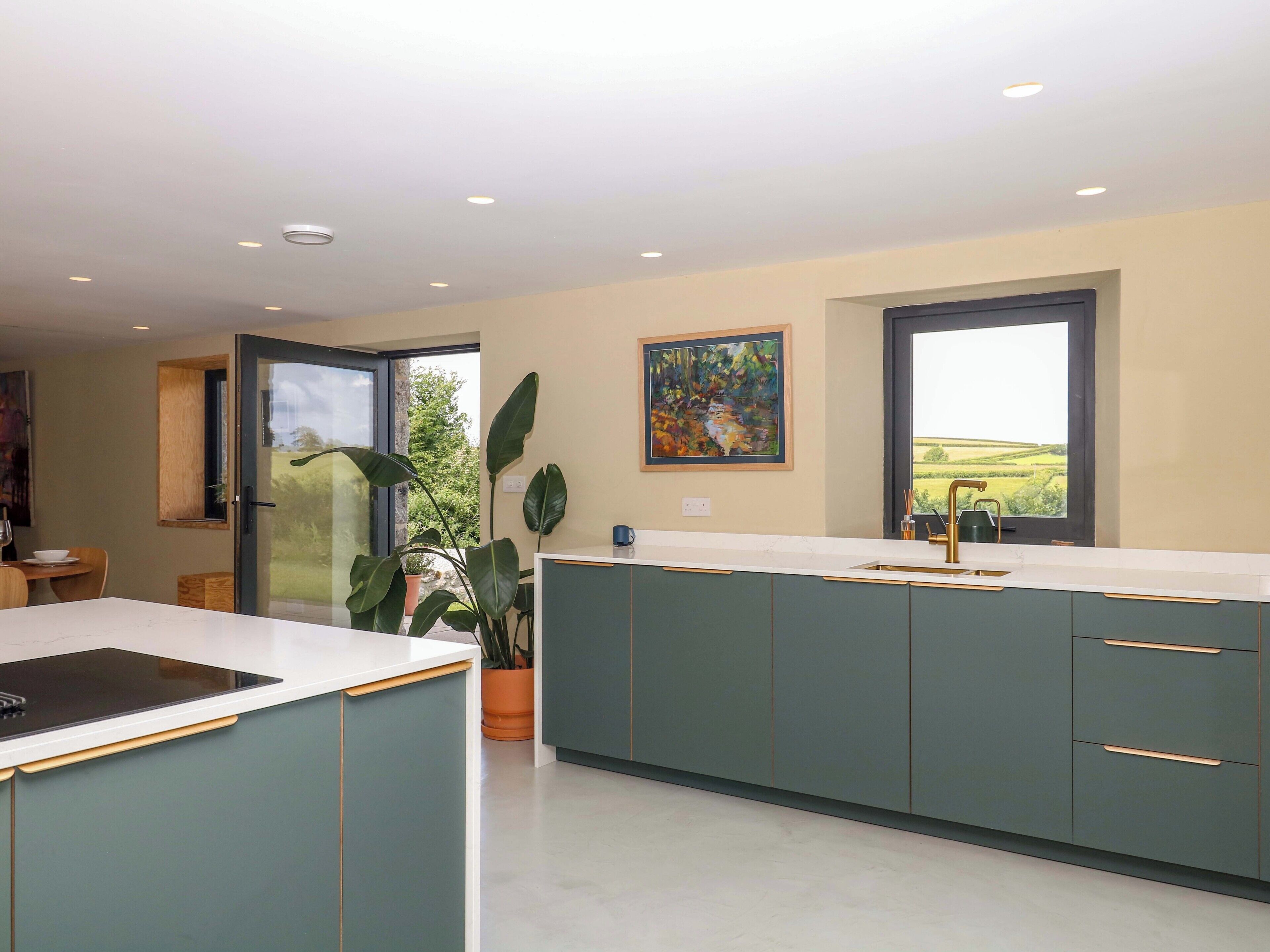 A modern kitchen with a large island, a dining area with a table and chairs, and a large window with a view of the countryside.