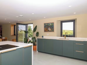 Una cocina moderna con una isla grande, una zona de comedor con mesa y sillas, y un ventanal con vistas al campo.