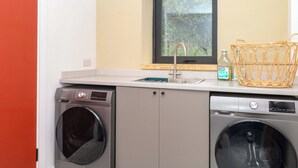 Un espace buanderie compact comprenant un lave-linge, un sèche-linge, un évier et une fenêtre.