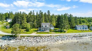 A coastal property with a main house, a garage, and a small guest house, surrounded by dense forest and rocky shoreline. - Island View Cottage - NEW! Waterfront Home in LDI (Little Deer Isle)