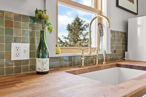 A kitchen with a wooden countertop, a green bottle, a window, and a gold faucet. - Island View Cottage - NEW! Waterfront Home in LDI (Little Deer Isle)