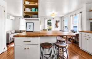 A kitchen with a wooden countertop, bar stools, a hanging light fixture, and a view of the outdoors. - Island View Cottage - NEW! Waterfront Home in LDI (Little Deer Isle)
