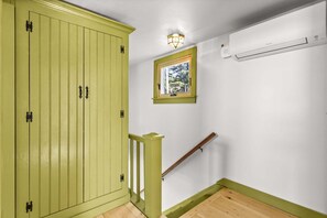 A room with a green cabinet, a small window with a view, a wooden handrail, and an air conditioning unit.