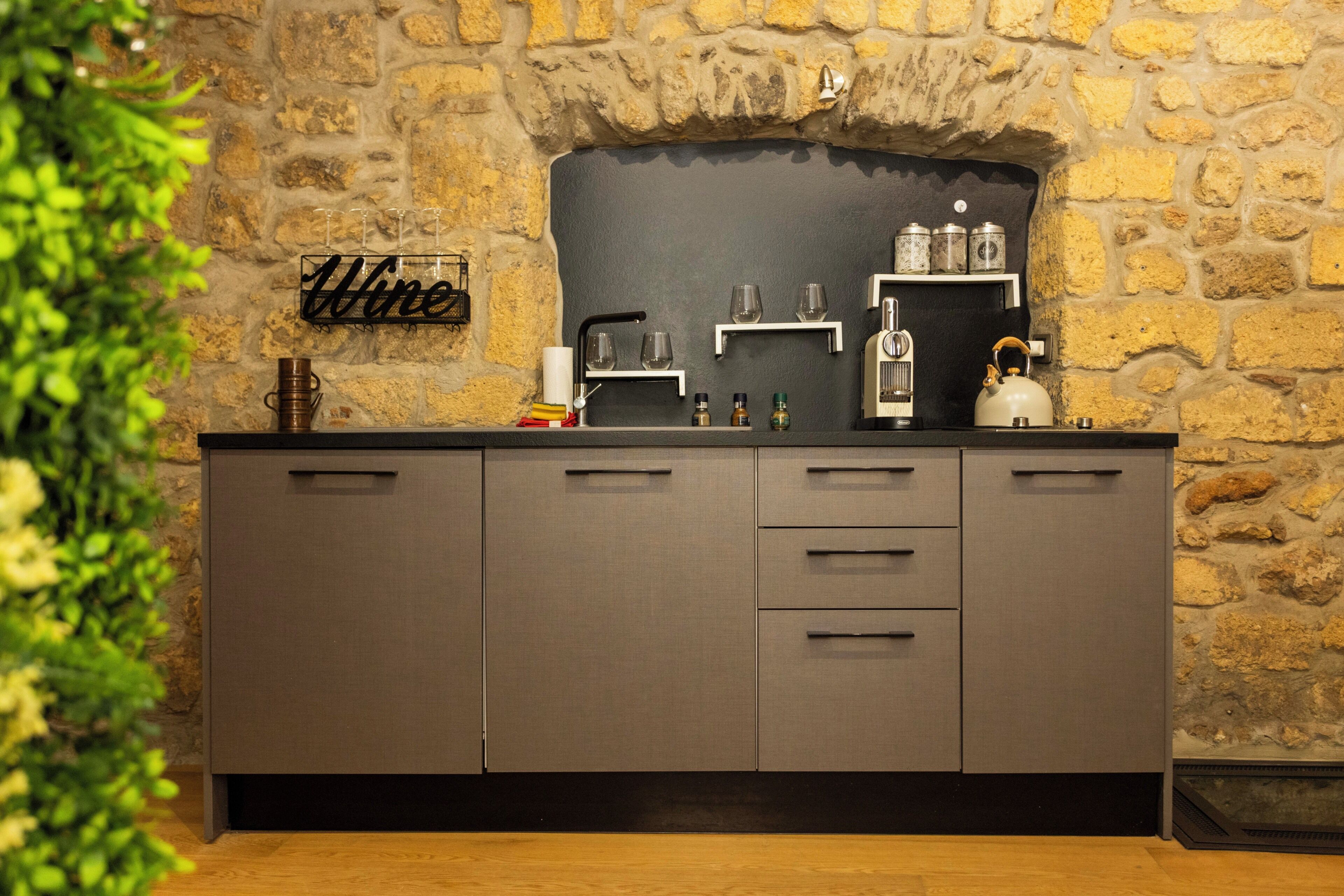 A kitchen with a stone wall, a black backsplash, and a sign that reads 'Wine'.