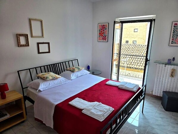 A bedroom with a bed, a nightstand, a window, and a balcony.