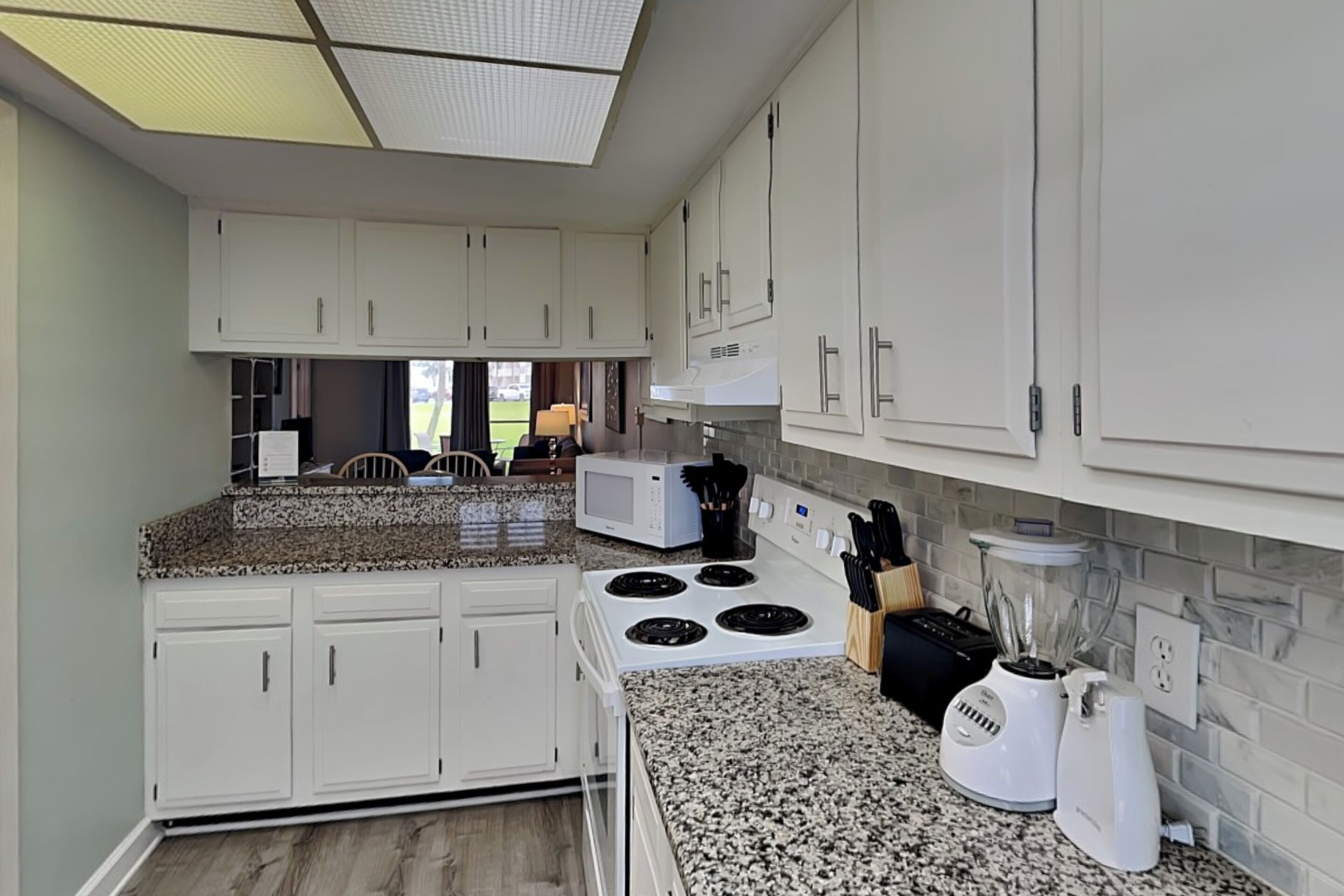A kitchen with white cabinets, a granite countertop, a stove, a microwave, a blender, and a coffee maker.