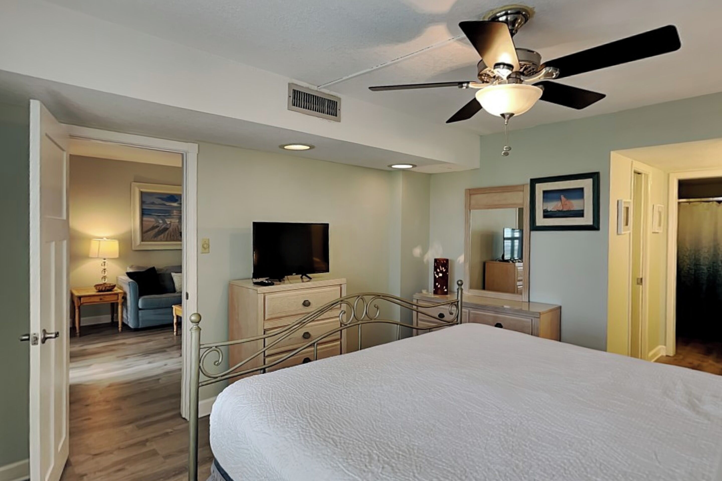 A bedroom with a bed, a ceiling fan, a television, a dresser, and a mirror.
