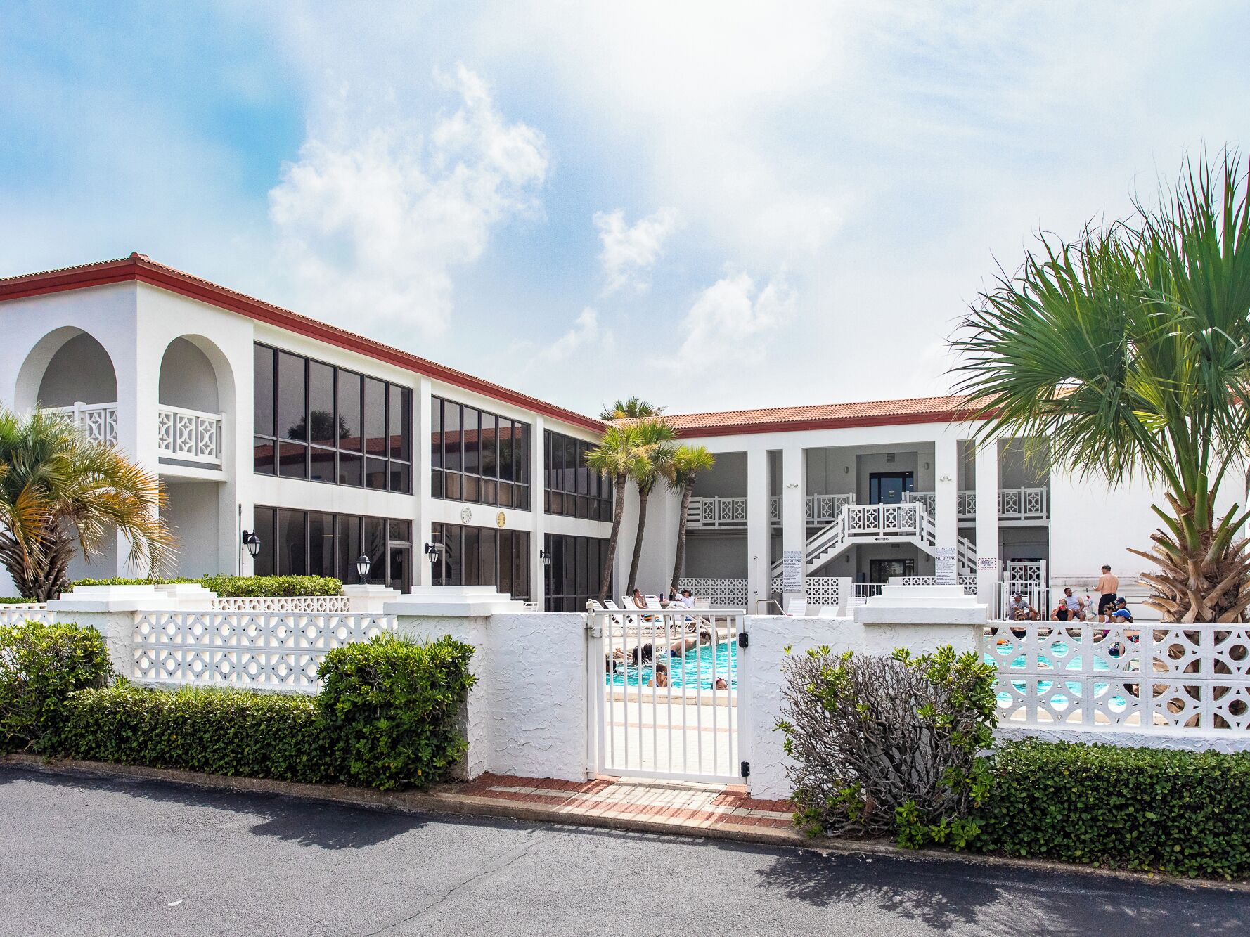 A two-story building with large windows, a swimming pool, and a gated entrance.