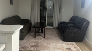 Een woonkamer met een bank, een salontafel, een zwarte lederen fauteuil en een schuifpui.