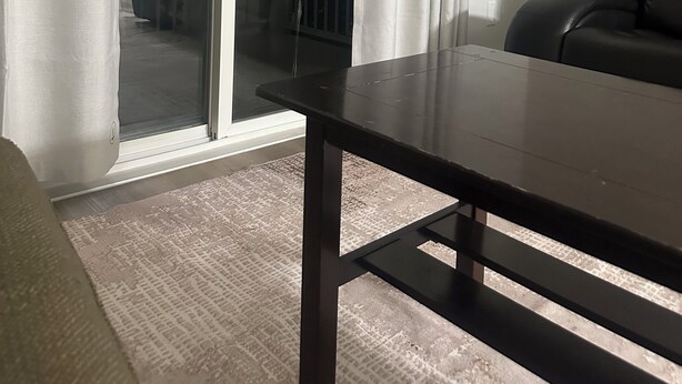Een kamer met een schuifdeur naar een balkon, een donker houten tafel en een zwarte leren stoel.