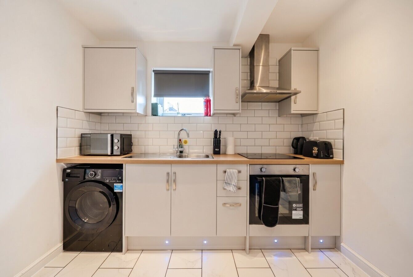 A compact kitchen with a washing machine, microwave, oven, and a window with a view.