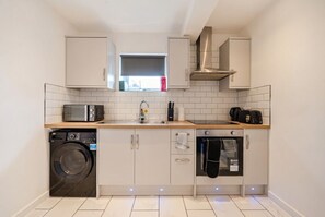 Een compacte keuken met een wasmachine, magnetron, oven en een raam met uitzicht.