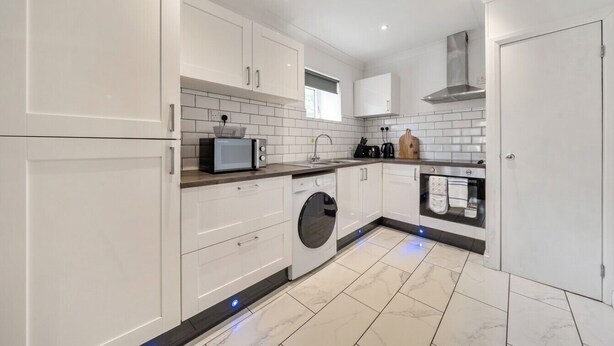 A modern kitchen with white cabinets, a washing machine, and a microwave. - 2-Bed Flat in Newsome · Sleeps 4 · Gated Parking near Castle Hill (Newsome)