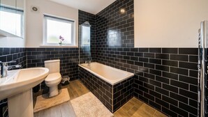 Une salle de bain avec des murs recouverts de carreaux noirs, un lavabo blanc, des toilettes et une baignoire.