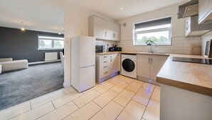 Une cuisine moderne avec des meubles blancs, un lave-linge encastré et une grande fenêtre qui laisse entrer la lumière naturelle.