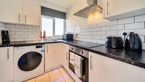 Una cocina moderna con armarios blancos, lavadora integrada, microondas, tostadora y campana extractora de acero inoxidable.