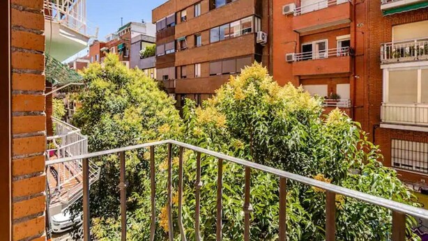 A multi-story residential building with balconies, a metal railing, and dense green foliage in the foreground. - Central, bright, and quiet (Madrid)